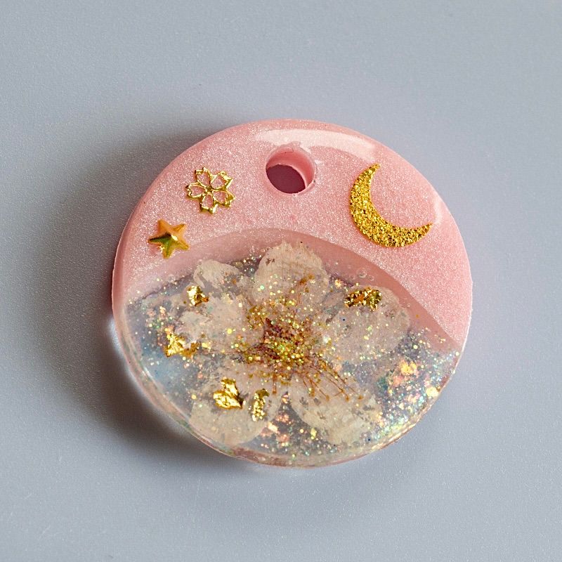 A picture of Hundemarke mit einer echten Kirschblüte und Glitzerakzenten. Mond und Sterne sowie feines Blattgold bringen einen zauberhaften Look. In rosa oder blau erhältlich und limitiert auf insgesamt vier Stück (jeweils eine Marke für Version A, B, C und D).