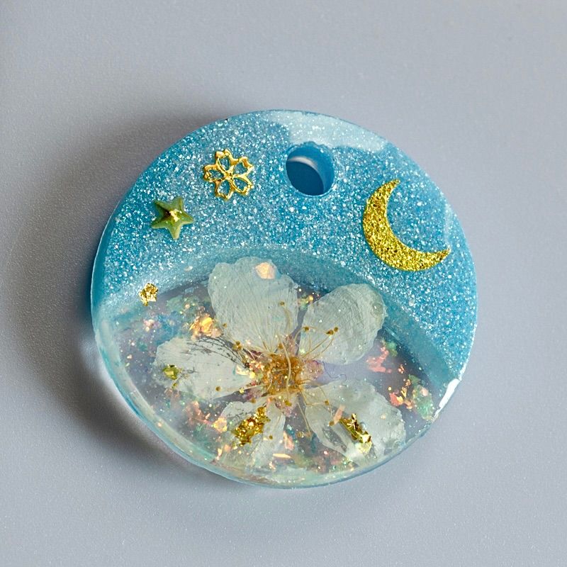 A picture of Hundemarke mit einer echten Kirschblüte und Glitzerakzenten. Mond und Sterne sowie feines Blattgold bringen einen zauberhaften Look. In rosa oder blau erhältlich und limitiert auf insgesamt vier Stück (jeweils eine Marke für Version A, B, C und D).