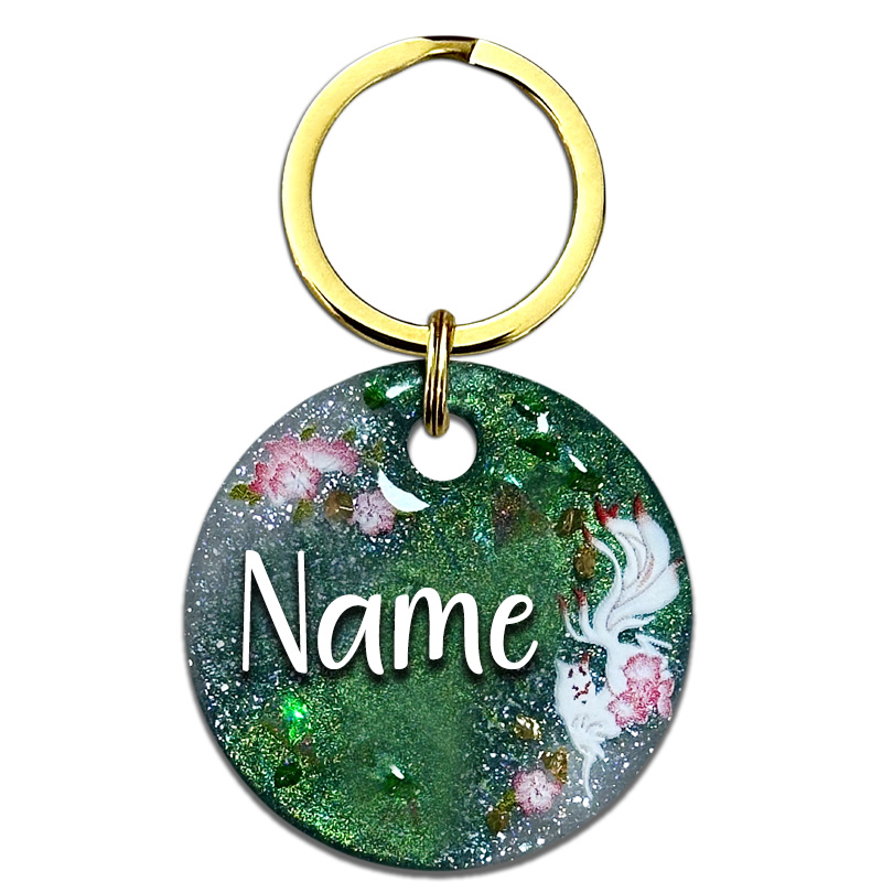 A picture of Die japanische Mythologie ist bekannt für viele Geister und Gottheiten. Inari ist eine japanische Fuchsgottheit des Shintoismus. Vor smaragdgrünem Perlpigment mit weißen, glitzernden Akzenten umspielt der weiße Fuchs rosafarbene Kirschblüten. Funkelnde Highlights aus goldenen und grünen Glitzersteinen runden das Design ab.